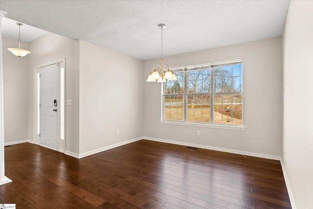 spare room featuring dark wood-type flooring, a textured ceiling, and a notable chandelier