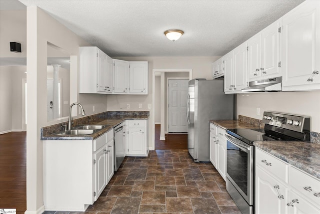 kitchen with appliances with stainless steel finishes, decorative columns, sink, white cabinets, and a textured ceiling