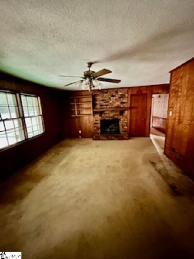 unfurnished living room with a fireplace, wood walls, a textured ceiling, and carpet