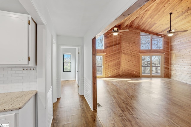 interior space featuring high vaulted ceiling, wood walls, beamed ceiling, wooden ceiling, and light wood-type flooring