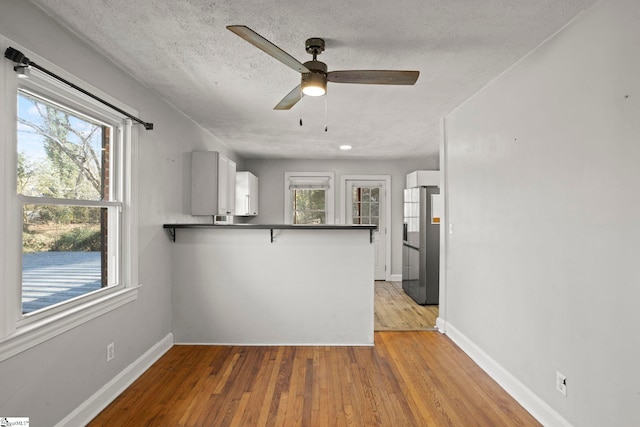 kitchen featuring light hardwood / wood-style flooring, stainless steel fridge, a textured ceiling, white cabinets, and kitchen peninsula