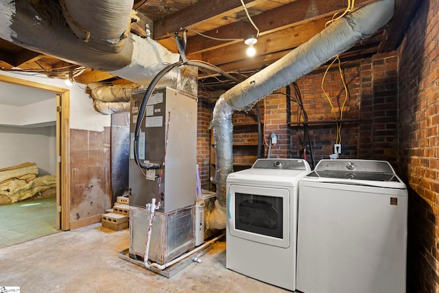 washroom with heating unit, washing machine and clothes dryer, and brick wall