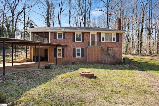 view of front facade with a fire pit, a carport, a sunroom, central air condition unit, and a front lawn