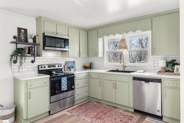 kitchen with green cabinetry, stainless steel appliances, sink, and backsplash