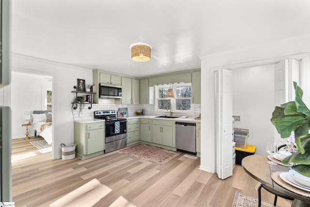 kitchen with sink, green cabinetry, light hardwood / wood-style flooring, appliances with stainless steel finishes, and backsplash