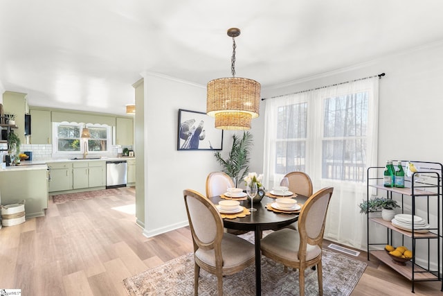 dining area featuring sink, ornamental molding, light hardwood / wood-style floors, and a chandelier