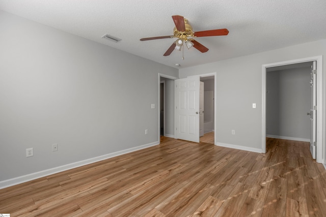 unfurnished bedroom featuring a walk in closet, a textured ceiling, a closet, ceiling fan, and light hardwood / wood-style floors