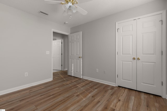 unfurnished bedroom with a textured ceiling, wood-type flooring, a closet, and ceiling fan