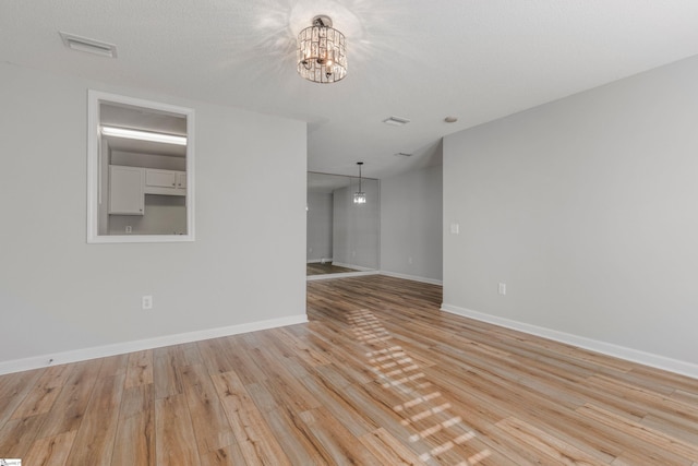 spare room with an inviting chandelier, a textured ceiling, and light wood-type flooring