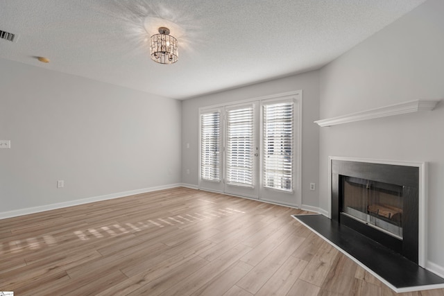 unfurnished living room featuring an inviting chandelier, light hardwood / wood-style floors, and a textured ceiling