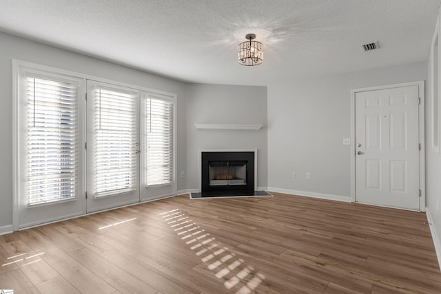 unfurnished living room with a chandelier, light hardwood / wood-style flooring, and a textured ceiling