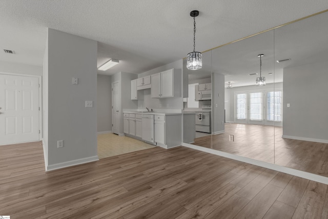 kitchen with white cabinetry, hanging light fixtures, white appliances, a textured ceiling, and light hardwood / wood-style flooring