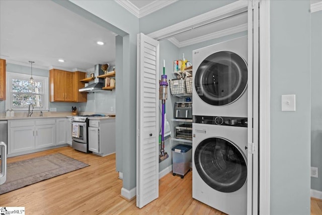 washroom featuring ornamental molding, stacked washer and clothes dryer, sink, and light wood-type flooring