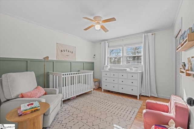 bedroom featuring crown molding, a nursery area, ceiling fan, and light wood-type flooring