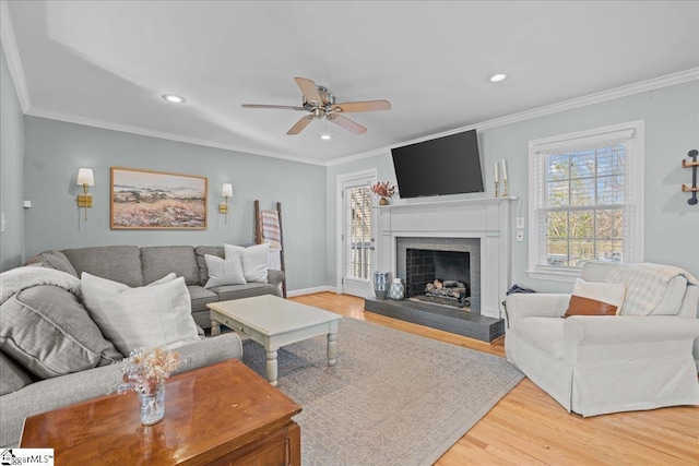 living room featuring ceiling fan, ornamental molding, wood-type flooring, and a brick fireplace