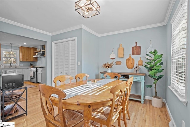 dining area featuring an inviting chandelier, sink, crown molding, and light hardwood / wood-style floors