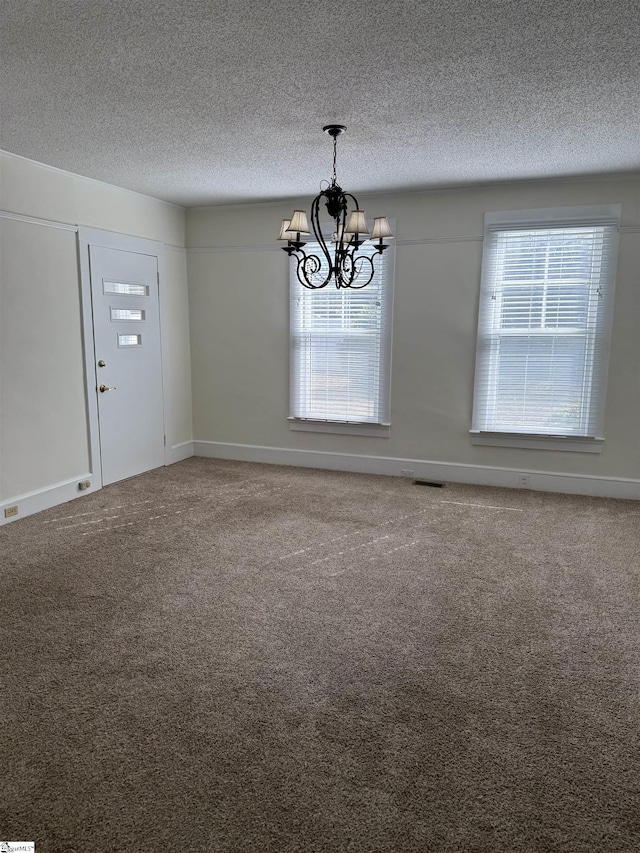 unfurnished dining area featuring an inviting chandelier, carpet floors, and a textured ceiling