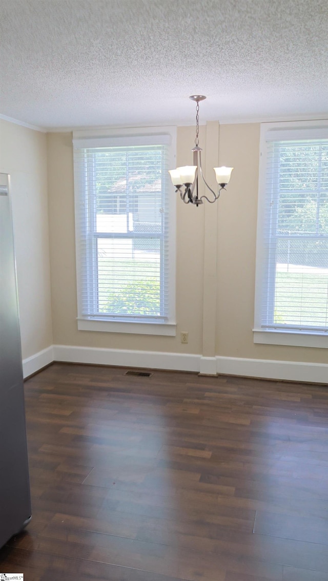 unfurnished dining area with a notable chandelier, a textured ceiling, dark wood-type flooring, and a healthy amount of sunlight