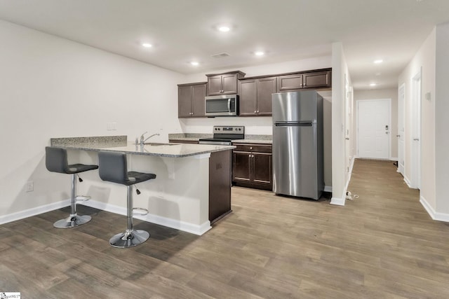 kitchen featuring appliances with stainless steel finishes, hardwood / wood-style floors, sink, dark brown cabinetry, and kitchen peninsula