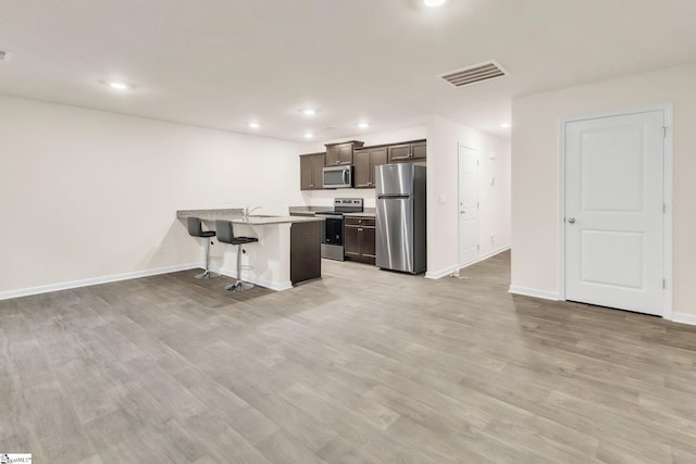 kitchen featuring appliances with stainless steel finishes, dark brown cabinets, a kitchen breakfast bar, a center island with sink, and light wood-type flooring