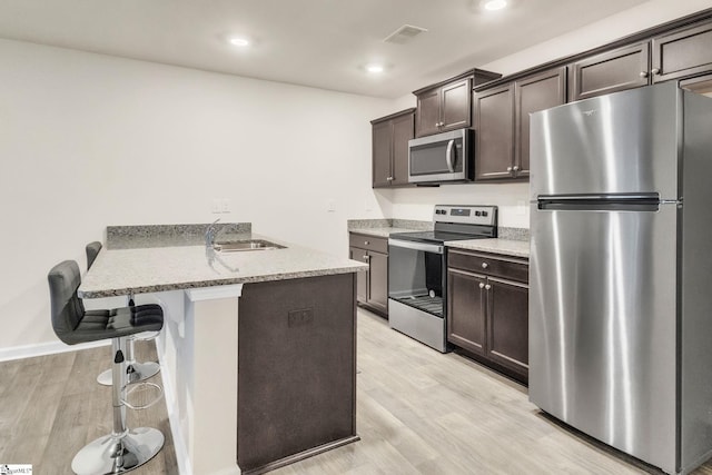 kitchen featuring sink, light wood-type flooring, appliances with stainless steel finishes, a kitchen breakfast bar, and kitchen peninsula