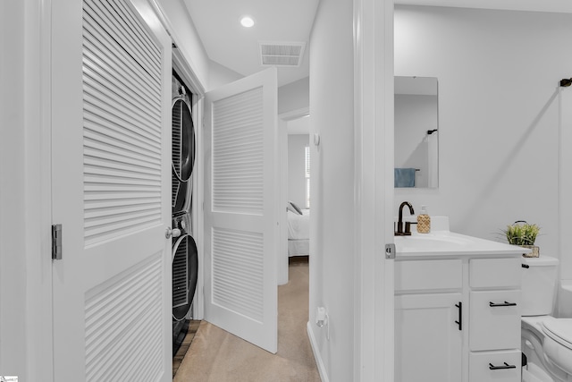 washroom featuring light colored carpet, stacked washing maching and dryer, and sink