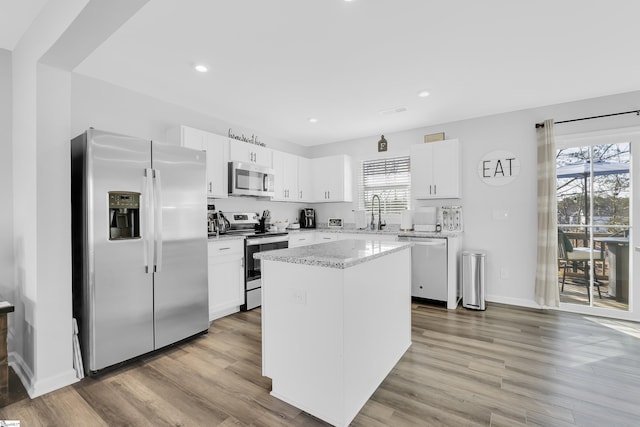 kitchen featuring a kitchen island, appliances with stainless steel finishes, white cabinetry, light stone counters, and light hardwood / wood-style flooring