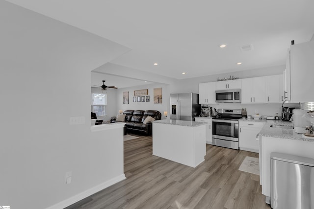 kitchen featuring light stone countertops, appliances with stainless steel finishes, white cabinets, and light wood-type flooring