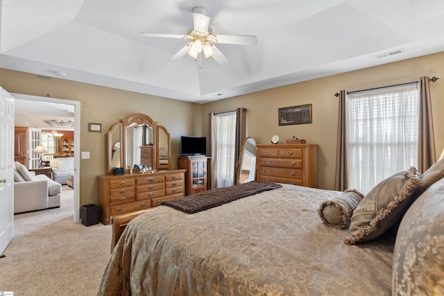 bedroom featuring light carpet, ceiling fan, and a tray ceiling