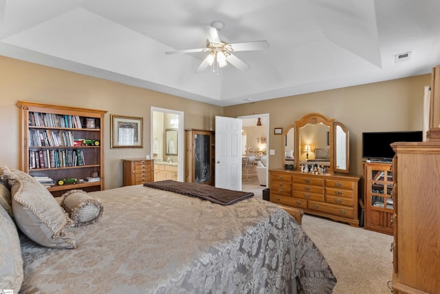 bedroom featuring ceiling fan, ensuite bath, carpet flooring, and a raised ceiling