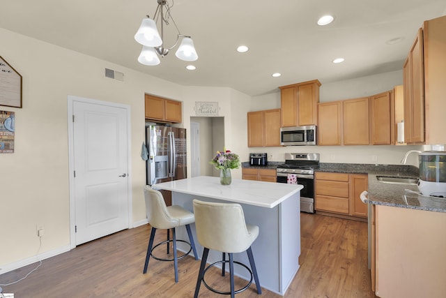 kitchen with sink, appliances with stainless steel finishes, a center island, wood-type flooring, and decorative light fixtures