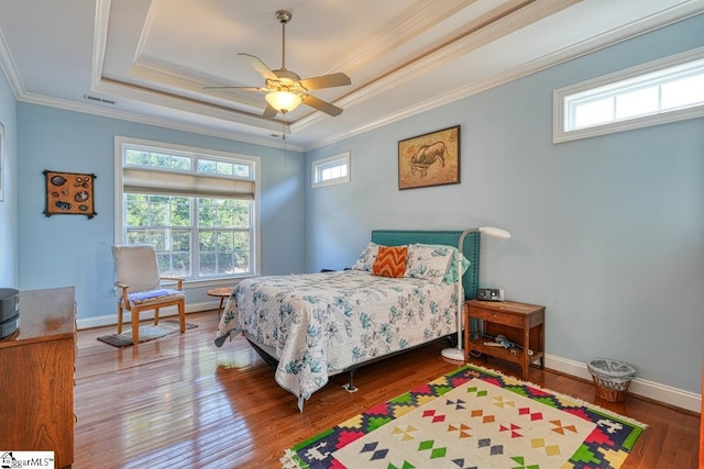 bedroom with wood-type flooring, ornamental molding, ceiling fan, and a tray ceiling