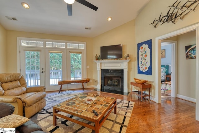 living room with french doors, lofted ceiling, light hardwood / wood-style flooring, ceiling fan, and a high end fireplace