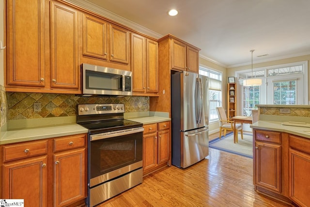 kitchen featuring appliances with stainless steel finishes, pendant lighting, backsplash, crown molding, and light hardwood / wood-style flooring