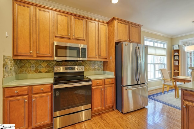 kitchen with crown molding, appliances with stainless steel finishes, decorative backsplash, and light wood-type flooring