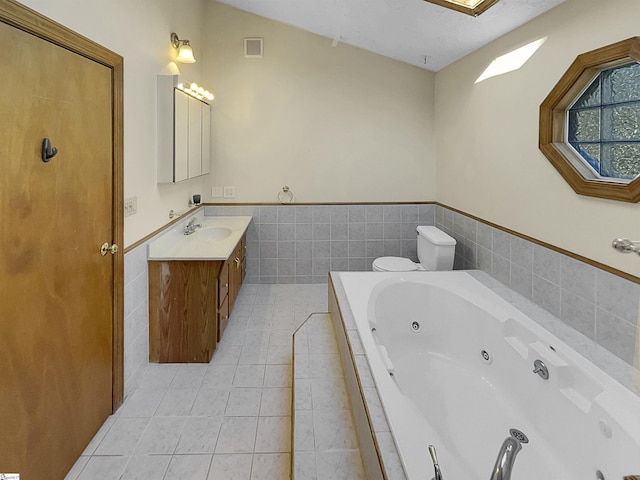 bathroom featuring toilet, tile walls, vanity, tiled tub, and tile patterned flooring