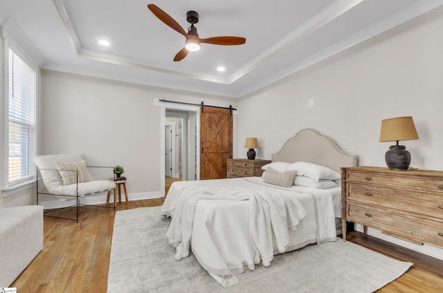 bedroom featuring crown molding, light hardwood / wood-style flooring, a raised ceiling, ceiling fan, and a barn door