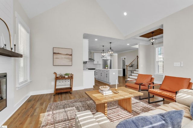 living room with a large fireplace, high vaulted ceiling, light hardwood / wood-style flooring, and a notable chandelier