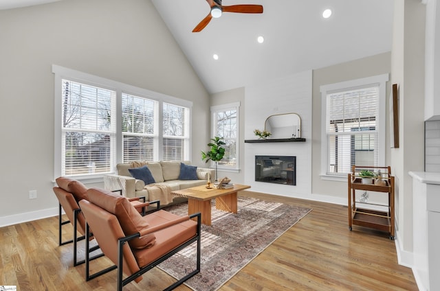 living room featuring a healthy amount of sunlight, high vaulted ceiling, a large fireplace, and light wood-type flooring