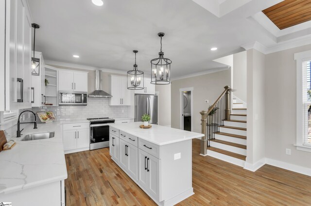 kitchen with sink, appliances with stainless steel finishes, a center island, white cabinets, and wall chimney exhaust hood