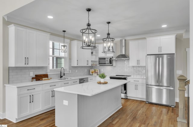 kitchen with white cabinetry, decorative light fixtures, appliances with stainless steel finishes, a kitchen island, and wall chimney range hood