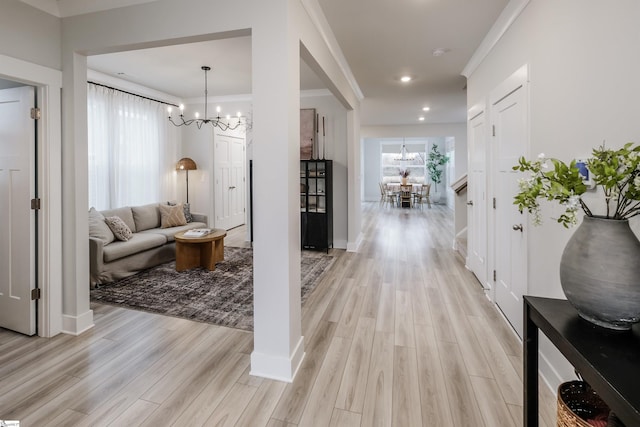 corridor with crown molding, a chandelier, and light hardwood / wood-style floors