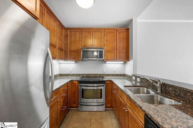 kitchen with appliances with stainless steel finishes, sink, light tile patterned floors, and dark stone counters