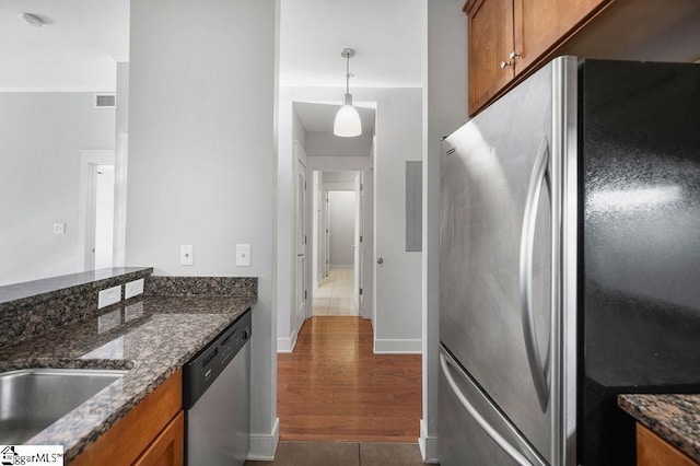 kitchen featuring stainless steel appliances, hanging light fixtures, dark wood-type flooring, and dark stone counters