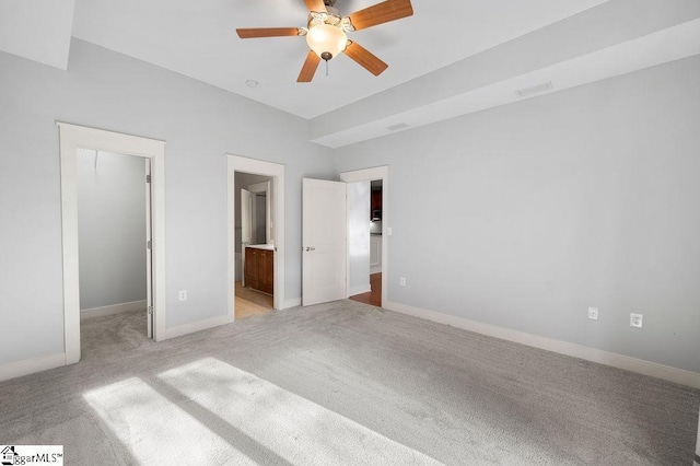 unfurnished bedroom featuring ensuite bath, a spacious closet, light carpet, a closet, and ceiling fan