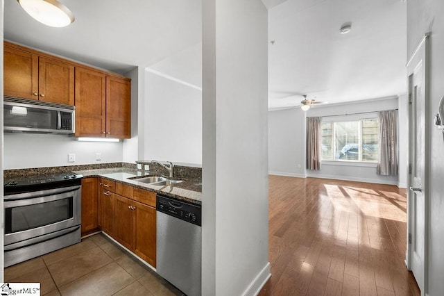 kitchen with sink, ceiling fan, appliances with stainless steel finishes, dark stone countertops, and hardwood / wood-style floors