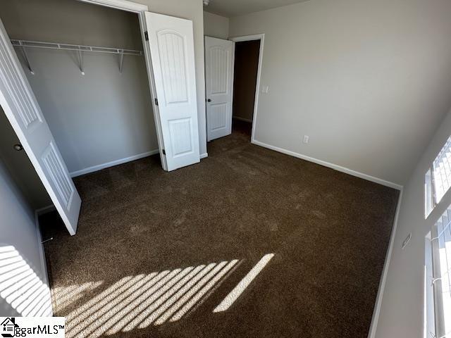 unfurnished bedroom with dark colored carpet and a closet