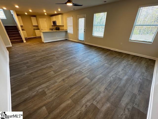 unfurnished living room featuring dark wood-type flooring and ceiling fan