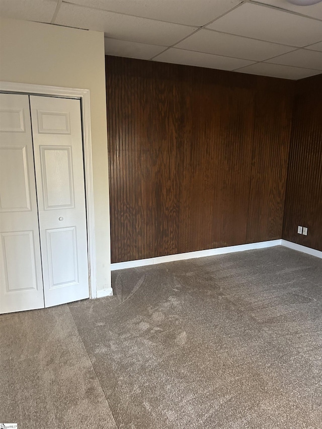 carpeted empty room with wooden walls and a paneled ceiling