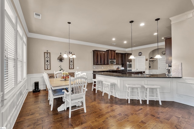 kitchen featuring appliances with stainless steel finishes, pendant lighting, ornamental molding, dark wood-type flooring, and dark brown cabinets